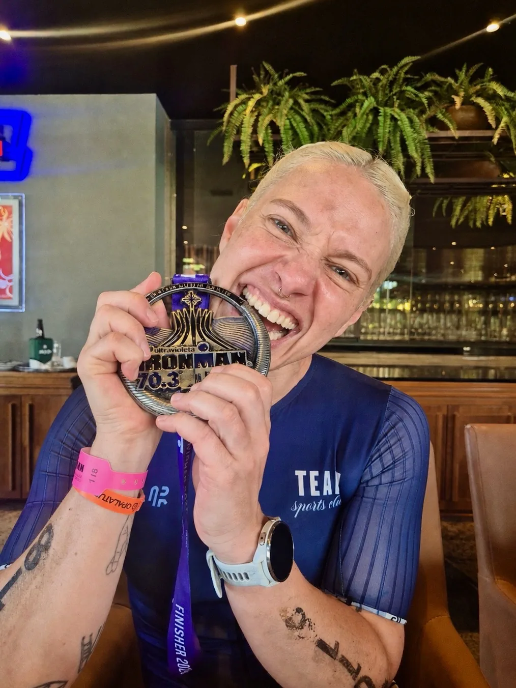 Zoe beißt lachend in die Ironman 70.3 Finisher-Medaille